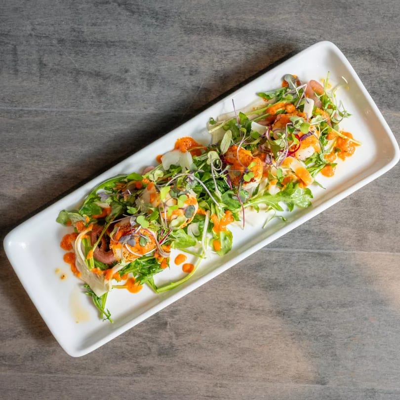 A vibrant salad with greens, shrimp, and orange dressing on a white rectangular plate.