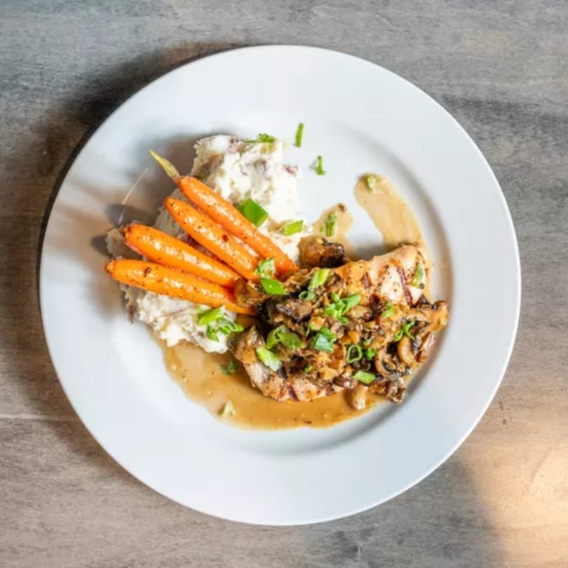 Chicken with mushroom sauce, mashed potatoes, and roasted carrots on a white plate.