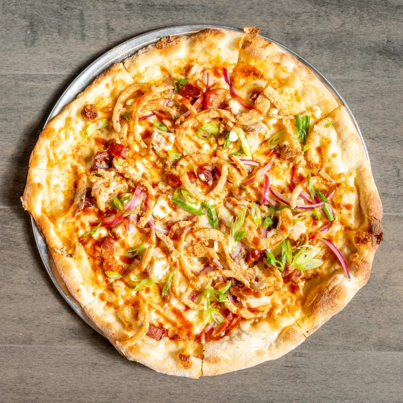 BBQ chicken pizza with crispy onions, red onions, and green onions on a metal pan.