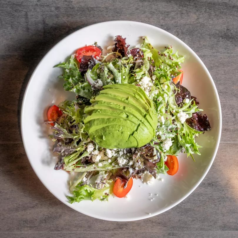 Fresh salad with mixed greens, cherry tomatoes, feta cheese, quinoa, and sliced avocado.