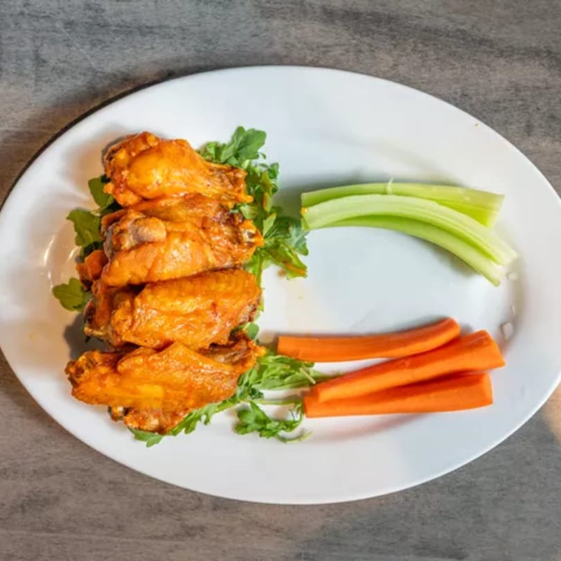 A plate of buffalo chicken wings with celery sticks, carrot sticks, and a bed of arugula.